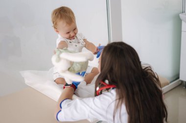 Yumuşak oyuncak tavşanı olan küçük bir hasta. Tıbbi klinikte gülümseyen genç bayan doktor..
