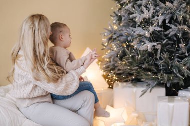 Annemin küçük oğluyla evde süslenmiş Noel ağacının portresi. Sevimli çocuk annesine tatil hazırlıklarında yardım ediyor..