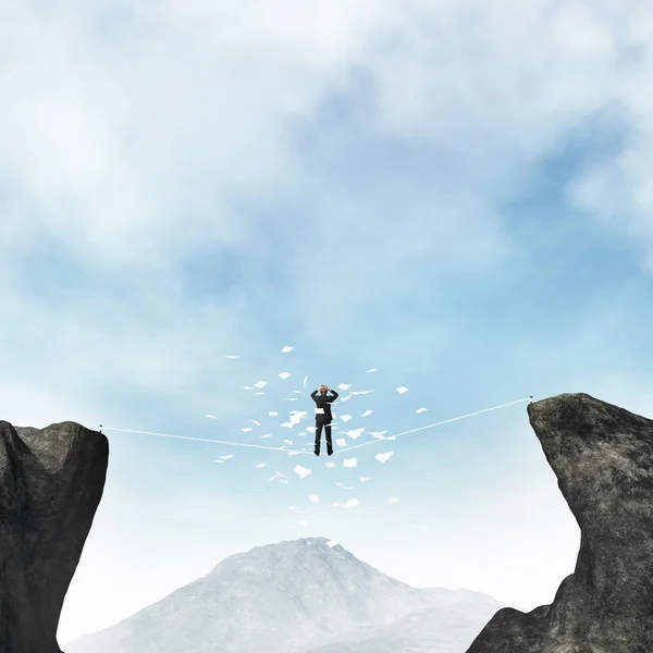 Businessman standing on a rope between mountains and drop out documents — Stock Photo, Image