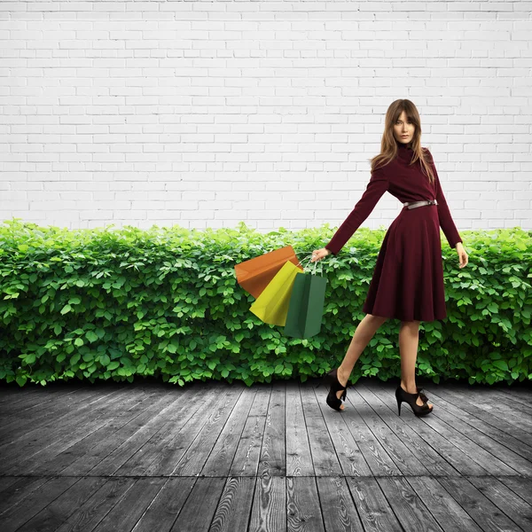 Женщина держит сумки для покупок у стен и кустов — стоковое фото