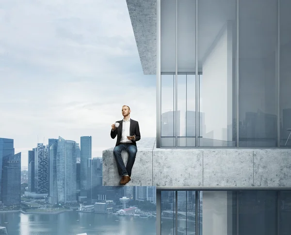 Businessman sitting on roof of skyscraper with cup of coffee — Stock Photo, Image