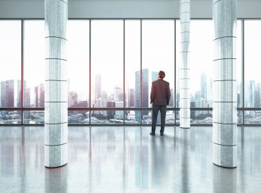 Büyük ofiste duran ve şehre bakan bir iş adamı.