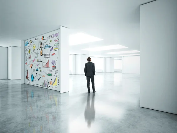Geschäftsmann steht in leerem Büro, Strategie an Wand ertränkt — Stockfoto