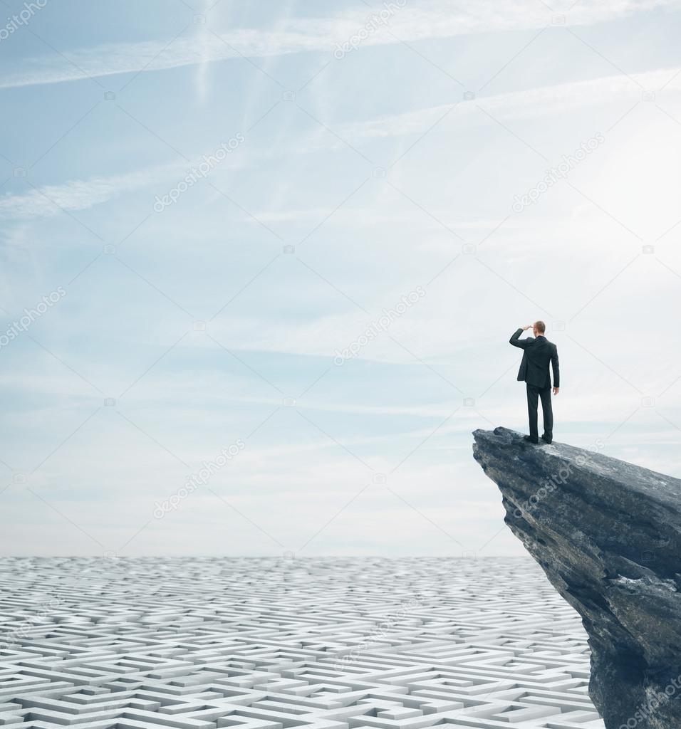 Businessman standing on a rock and looking at huge labyrinth