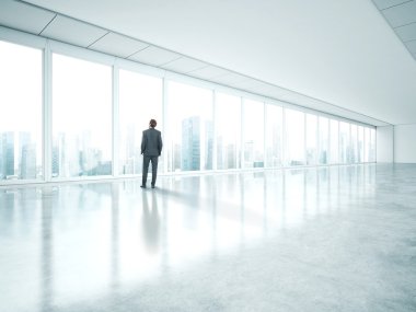 Businessman standing in empty bright office and look at city clipart
