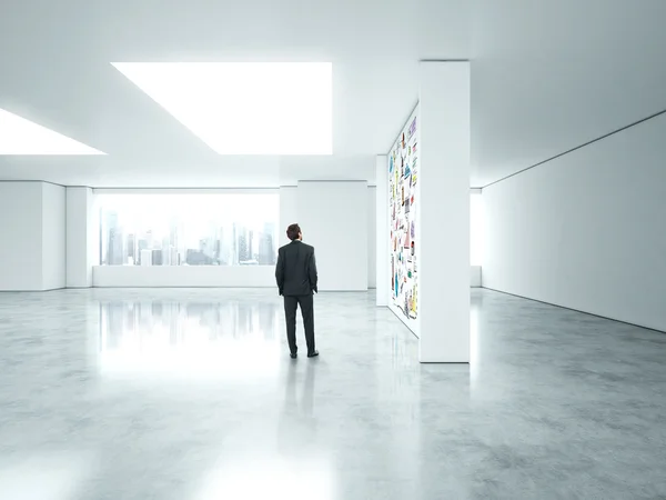 Geschäftsmann steht in leerem hellen Büro mit Geschäftsstrategie an der Wand — Stockfoto