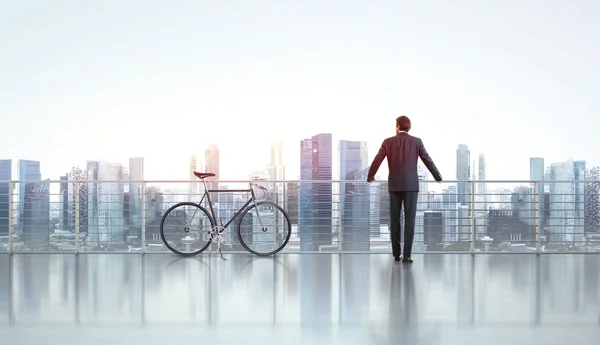 Businessman with bicycle looks at city — Stock Photo, Image