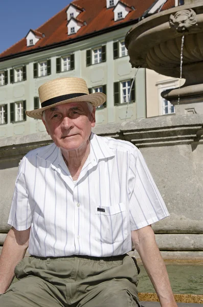 Senior sitting by fountain in summer day — Stock Photo, Image