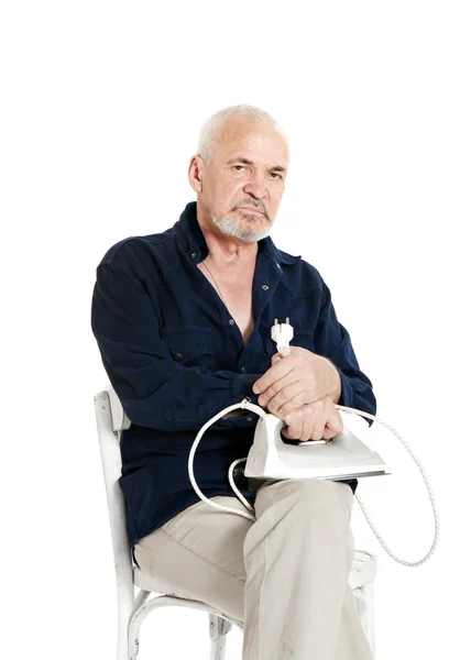 Mann sitzt auf einem Stuhl und hält elektrisches Bügeleisen — Stockfoto