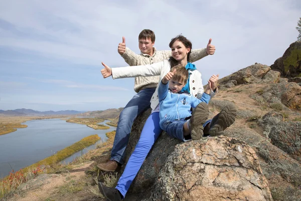 Happy family sitting on the stone and showing thumb — Stock Photo, Image