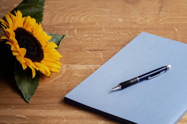 Ahşap masada mavi bir defter, kalem ve taze ayçiçeği ile yaratıcı yazım zamanı.