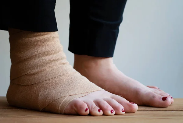 Feet of a person. Compression bandage around one foot due to a sprained ankle and injury.