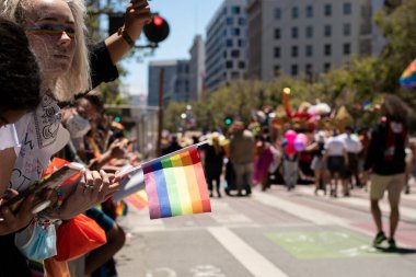 San Francisco, California, ABD - 26 Haziran 2022: Gökkuşağı göz makyajlı kişi, gururlu bir bayrak sallayarak kentteki geçit törenini izliyor. 