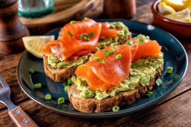 Lezzetli avokado ve füme somon tostları sade ahşap bir masanın üstünde..
