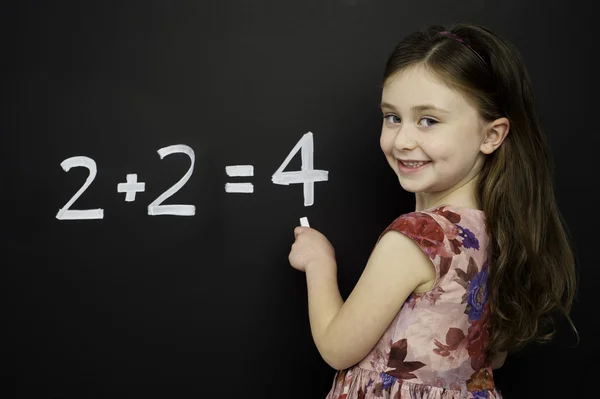 Smart young girl stood writing on a blackboard — Stock Photo, Image