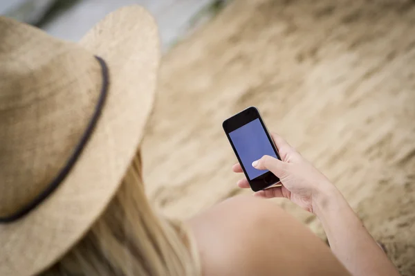 Donna seduta sulla spiaggia con un telefono cellulare Fotografia Stock