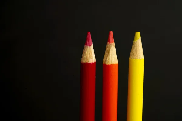 Red, orange and yellow coloured pencil crayons on a black backgr — Stock Photo, Image