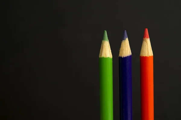 Green, purple and orange coloured pencil crayons on a black back — Stock Photo, Image