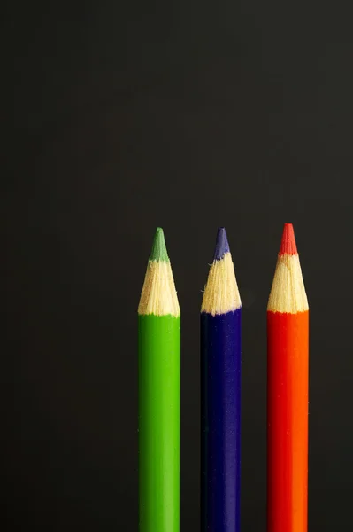 Green, purple and orange coloured pencil crayons on a black back — Stock Photo, Image