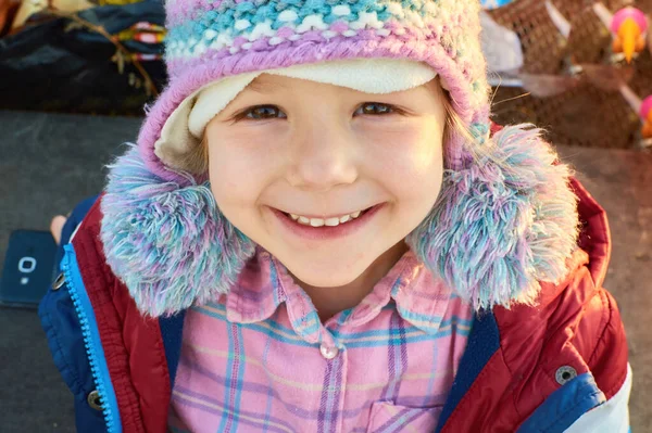 Une petite adolescente souriante avec un bonnet de fourrure dans une journée d'automne avec une lueur chaude — Photo