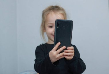 Cep telefonu kullanan mutlu, gülümseyen küçük bir kız çocuğu.