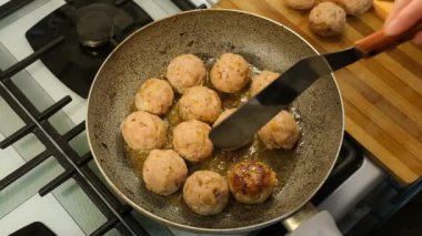 Kadın, sıcak yağlı tavada ev yapımı köfteleri ters çevirmek için spatula kullanıyor.