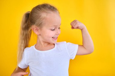strong shiny school girl showing arm muscles isolated yellow color background successful training workout