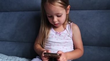 Küçük kız elinde akıllı telefon tutarak yatağa uzanıyor, interneti harcıyor, genç nesil alet bağımlısı, cihaz aşırı kullanımı kavramı