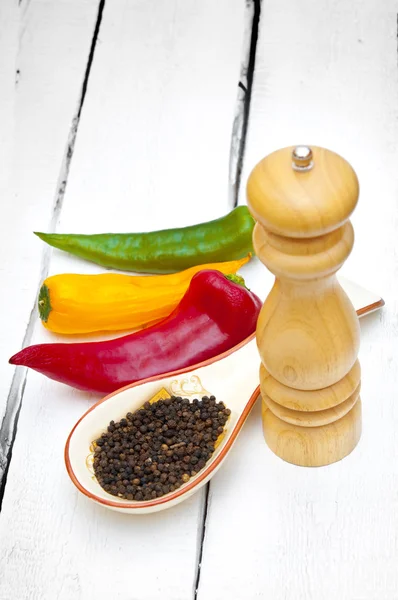 Peppers and pepper shaker on wooden backdrop — Stock Photo, Image