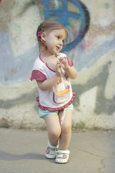 Verlegen Kid meisje met staartjes op een achtergrond van een betonnen muur met graffiti — Stockfoto