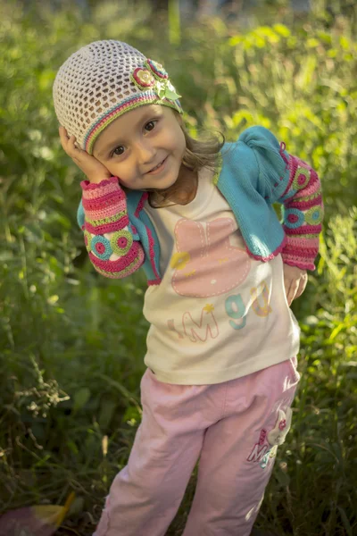 A flirty happy little girl tilted her head and touched her face with her hands. — Stock Photo, Image