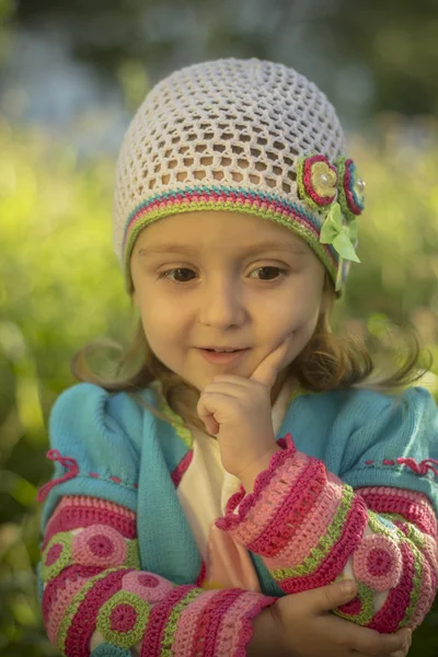 Ein neugieriges kleines Mädchen denkt, träumt oder denkt, einen Finger auf ihren Kopf. sie trägt einen Strickpullover und eine Mütze — Stockfoto