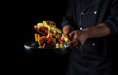 Profesyonel şef sebzeleri kızartma tavasında hazırlar. Sağlıklı vejetaryen yemekleri ve yemekleri karanlık bir arka planda pişirmek. Ücretsiz reklam alanı