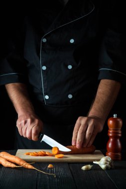 Şef restoranın mutfağında sebze çorbası için havuç kesiyor. İş sırasında aşçının ellerini yakın plan çek. Havuç diyeti