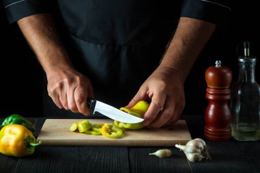Aşçı restoran mutfağında salata için dolmalık biber kesiyor. Çalışırken aşçı ellerinin yakın çekimi.