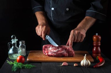 Profesyonel şef mutfakta bıçakla et keser ve yemek hazırlar. Bir restoranda lezzetli bir öğle yemeği hazırlamak için mutfak masasındaki sebze ve baharatlar.