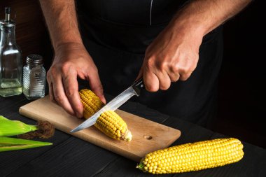 Aşçı taze mısırı bıçakla keser. Haşlanmış mısır kahvaltı ya da öğle yemeği için harika bir diyettir. Restoran mutfak masasında çalışma ortamı