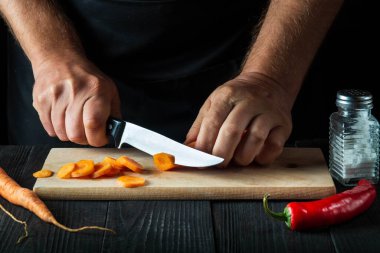 Profesyonel şef, restoranın mutfağında sebze çorbası için havuç kesiyor. İş sırasında aşçının ellerini yakın plan çek. Havuç öldü.