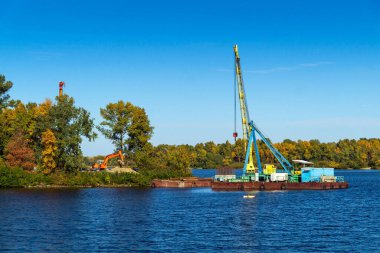 Nehir boyunca adaya giden bir köprü inşaatı başlıyor. Vinçli bir gölette mühendislik işi.