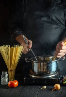 Profesyonel şef İtalyan makarnasını tencerede sebzeyle hazırlıyor. Lokanta mutfağında yemek pişirirken ellerin yakın plan çekimi.
