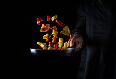 Profesyonel şef sebzeleri kızartma tavasında hazırlar. Sağlıklı vejetaryen yemekleri ve yemekleri karanlık bir arka planda pişirmek. Ücretsiz reklam alanı