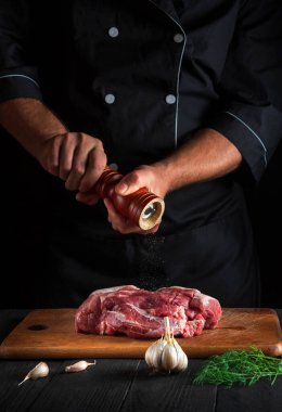 Profesyonel şef çiğ et fileto pişiriyor ve siyah arka planda salamura için biber ya da biber ekliyor. Restoranda ya da kafede, mutfakta çalışma ortamı