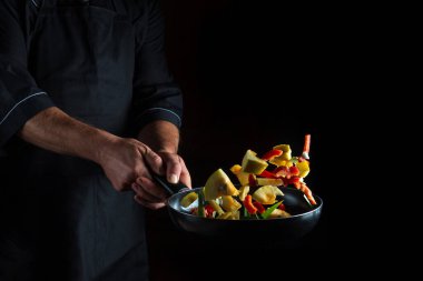 Şef kızartma tavasında sebze hazırlar. Sağlıklı vejetaryen yemekleri ve yemekleri karanlık bir arka planda pişirmek. Ücretsiz reklam alanı