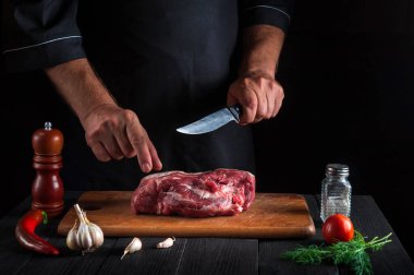 Aşçı mutfakta bıçakla et keser, yemek hazırlar. Lokantadaki mutfak masasında lezzetli bir yemek hazırlamak için sebze ve baharat var.