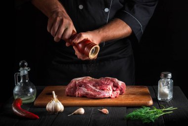 Şef çiğ et fileto pişiriyor ve siyah arkaplanda salamura yapmak için biber ya da biber ekliyor. Restoranda ya da kafede, mutfakta çalışma ortamı.