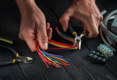 Bağlanmak için elektrik kabloları. Elektrikçi ustasının atölyesindeki elektrikli aletlerin tamiri. İş sırasında profesyonel ustanın ellerini yakın plan çek.