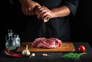 Şef çiğ et fileto pişiriyor ve siyah arkaplanda salamura yapmak için biber ya da kırmızı biber ekliyor. Restoranda ya da kafede, mutfakta çalışma ortamı