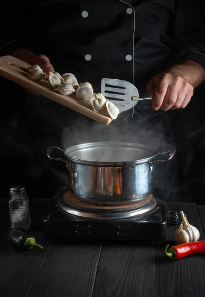 The chef cooks meat dumplings in a saucepan in the restaurant kitchen. Close-up of the hands of cook during work. Free advertising space