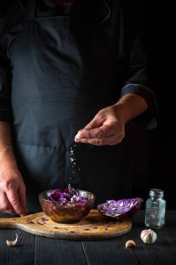 Şef salataya taze kırmızı lahana tuzu serper. Restoran mutfağında ahşap bir masada sağlıklı yemek hazırlığı.