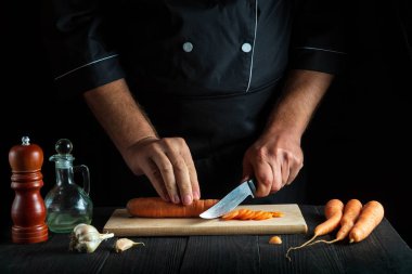 Mutfakta sebze çorbası için havuç kesen profesyonel bir aşçı. İş sırasında aşçının ellerini yakın plan çek. Havuç diyeti